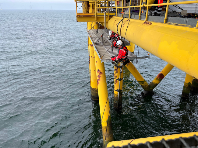 To rope access teknikere er i gang med at opsætte systemhængestilladser på jacket platform, for de kan begynde af sandblæse og male riggen. 